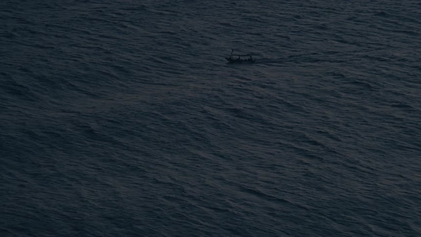 A lone fishing boat navigates the vast, dark, and choppy waters of the open ocean at twilight