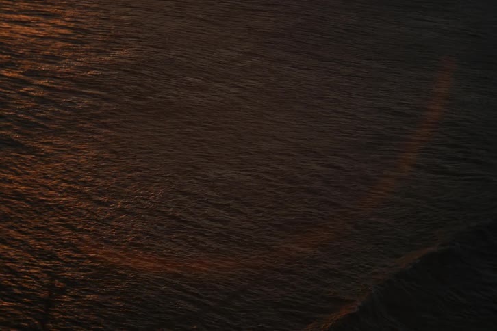 Abstract top-down view of the dark ocean surface with gentle ripples reflecting the warm golden light of a sunset