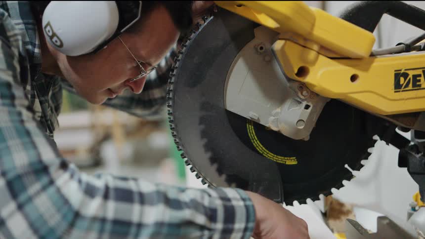 A focused craftsman in glasses and ear protection carefully sets up a miter saw for a precise cut in a workshop