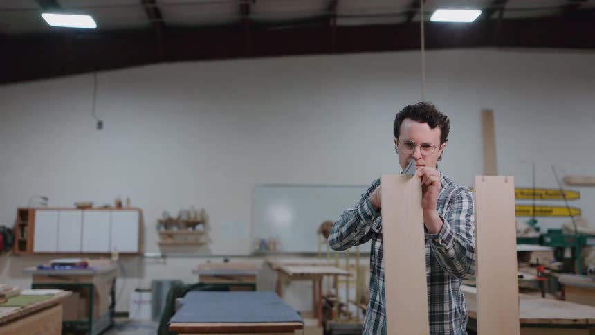 A focused woodworker in a flannel shirt carefully cuts a dovetail joint by hand in his spacious workshop