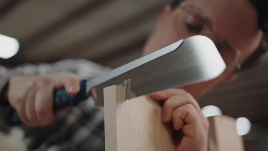 A focused woodworker meticulously cuts a joint into a wooden board using a traditional Japanese pull saw in his workshop