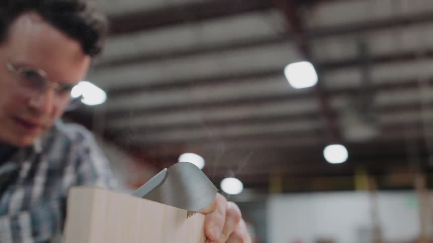 A skilled woodworker meticulously saws a piece of wood with a Japanese pull saw in a workshop, captured in slow motion