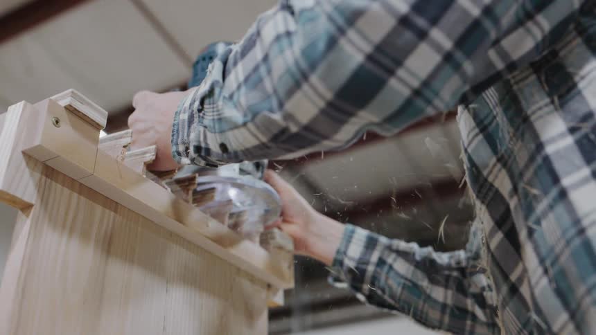 A carpenter in a workshop carefully uses a power router to cut dovetail joints into a wooden board in slow motion