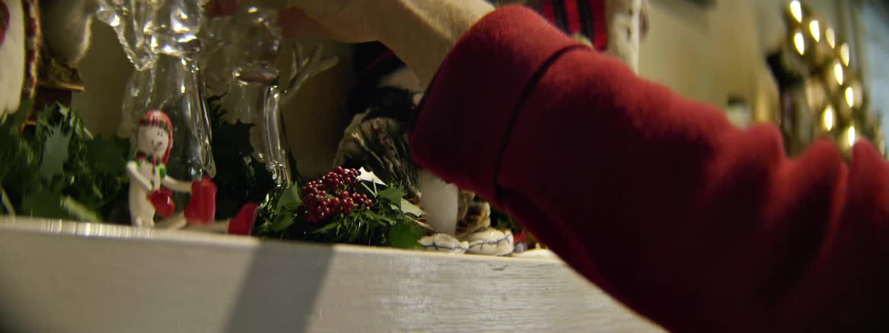 A woman decorates a fireplace mantle with christmas decorations