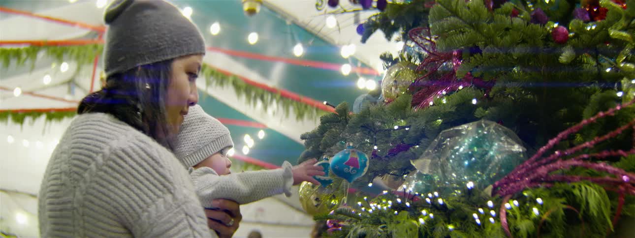 Baby held by woman looks at and touches ornament on christmas tree
