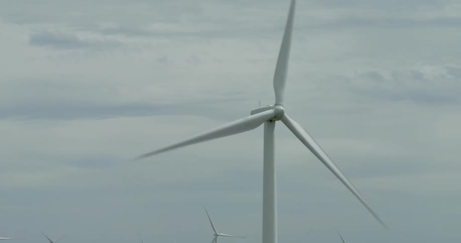 Close up of a massive wind turbine spinning its blades on a wind farm under an overcast sky