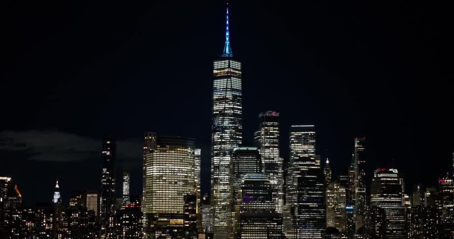 A beautiful nighttime view of the brightly lit Lower Manhattan skyline, featuring the World Trade Center, slowly zooms out