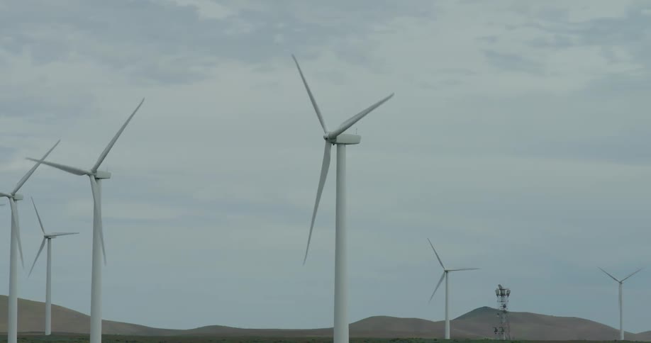 A wind farm with multiple turbines spinning to generate renewable energy on a vast, hilly landscape under an overcast sky