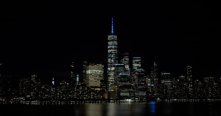 Stunning view of the illuminated Lower Manhattan skyline and One World Trade Center at night reflecting on the water