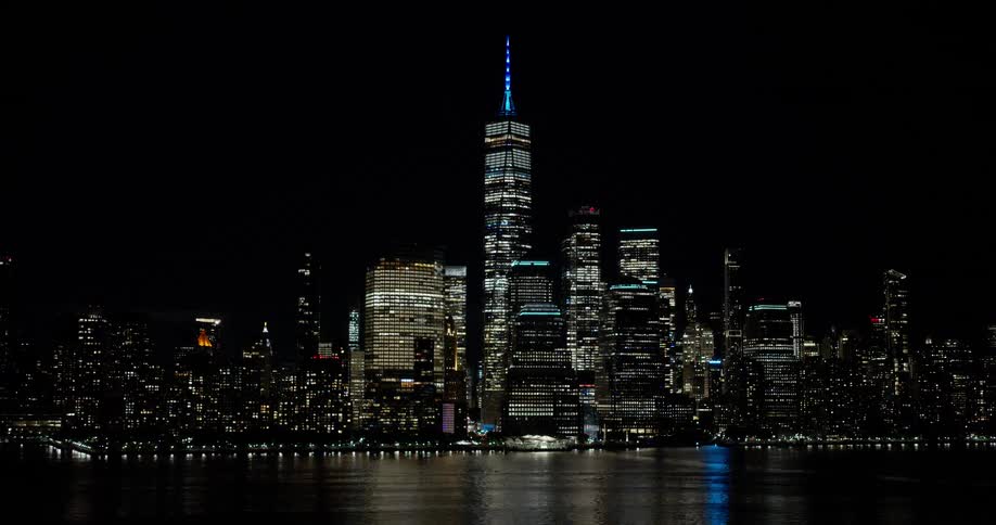 The iconic New York City skyline glows brightly at night, with the One World Trade Center standing tall against the dark sky