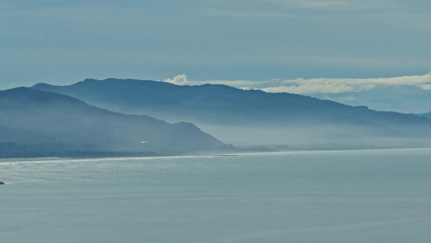 Layers of misty mountains meet the tranquil sea along a beautiful and expansive coastline