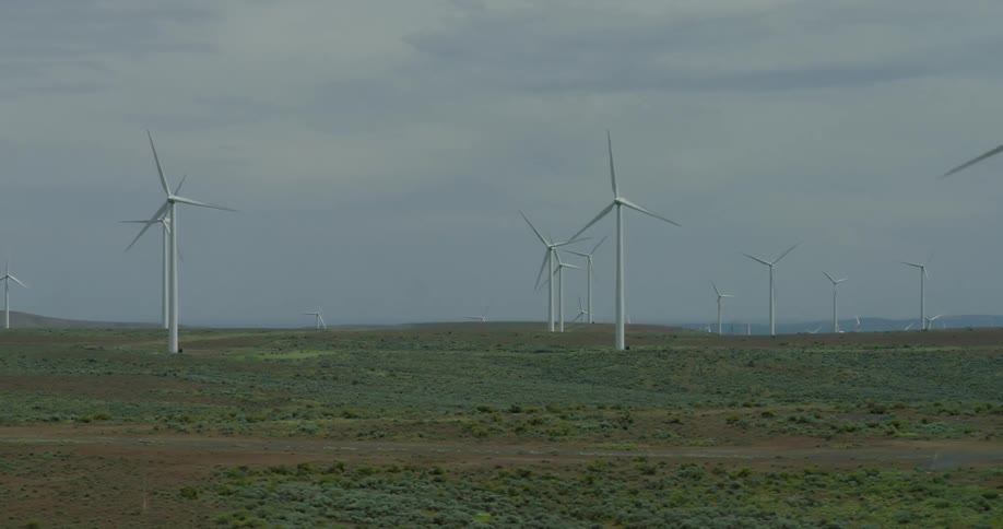 A large wind farm with numerous spinning turbines generating clean energy across a vast, open landscape under a cloudy sky