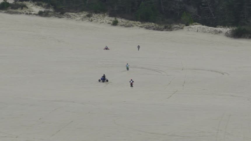 A group of people enjoys riding off-road vehicles across the sand dunes on an overcast day