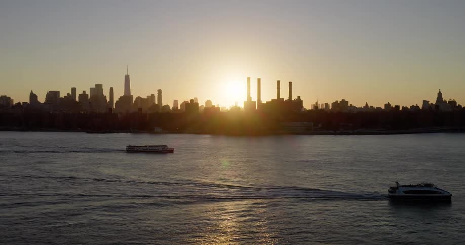 Ferries cruise along the East River with the iconic Manhattan skyline silhouetted by the golden glow of a beautiful sunset