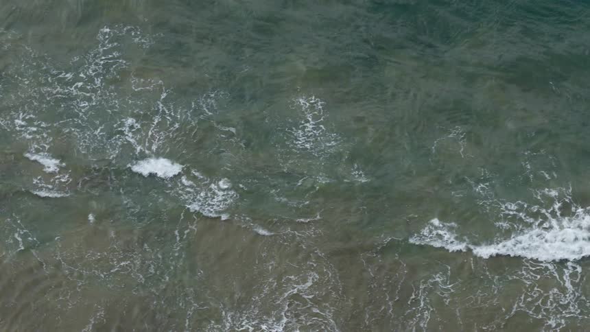 A serene top-down aerial view of tranquil ocean waves slowly washing onto a sandy beach