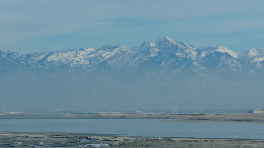 An aerial view slowly pulls back from the majestic snow-capped Wasatch mountain range towering over the Great Salt Lake in Utah