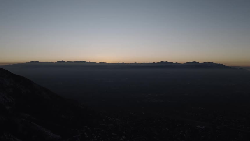A static, high-angle shot of a silhouetted mountain range against a clear pre-dawn sky, with a thick layer of haze covering the valley below