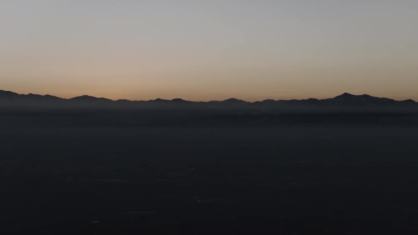 The silhouette of a distant mountain range is visible at dawn over a vast, dark valley covered in a blanket of fog