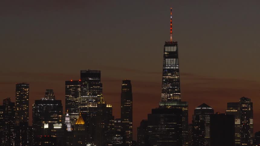 The iconic Lower Manhattan skyline, featuring the illuminated One World Trade Center, stands against a warm twilight sky