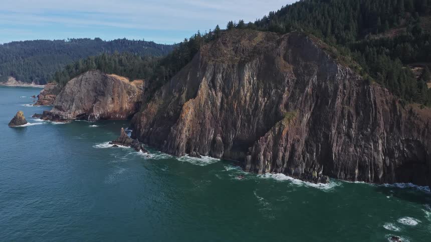 A majestic aerial view captures the dramatic cliffs of the rugged Pacific Northwest coastline, where the ocean meets dense evergreen forests