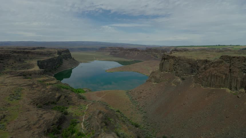 An aerial journey over a vast rocky canyon slowly reveals a tranquil hidden lake below