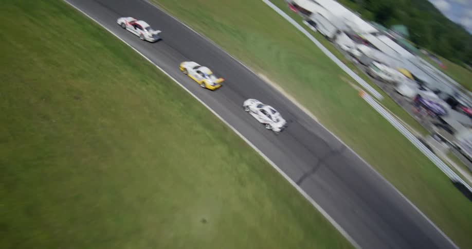 A dynamic aerial view follows three sports cars racing around a curve on a professional track on a sunny day