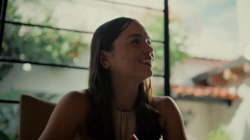 A young woman writing at a table looks up and breaks into a joyful smile and laughter during a conversation