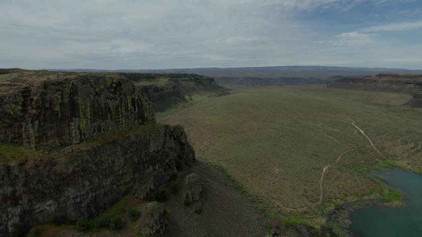 A stunning aerial flight over the dramatic cliffs and expansive valley of a remote, arid canyon next to a serene lake