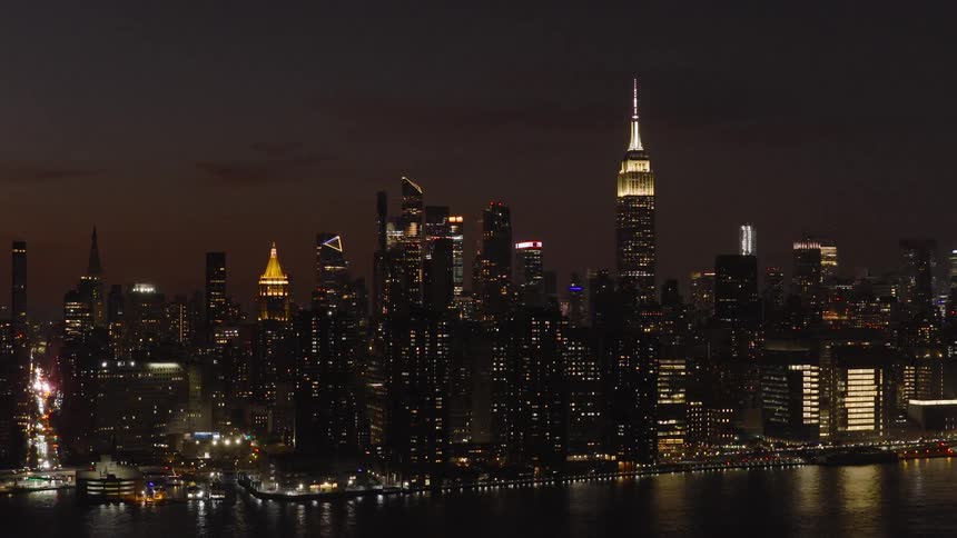 An evening aerial view of the iconic New York City skyline slowly pulling back to reveal the glowing cityscape and the Empire State Building