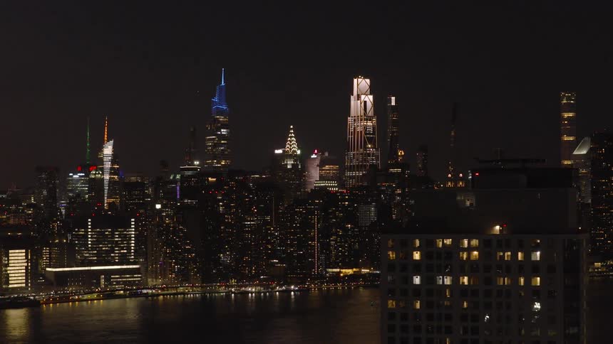 A majestic aerial tracking shot reveals the glittering Manhattan skyline at night, with a helicopter flying past iconic skyscrapers