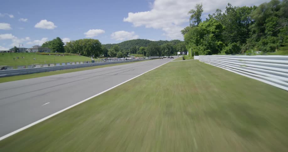 An exhilarating first-person view follows vintage open-wheel cars racing at high speed around a sunny track