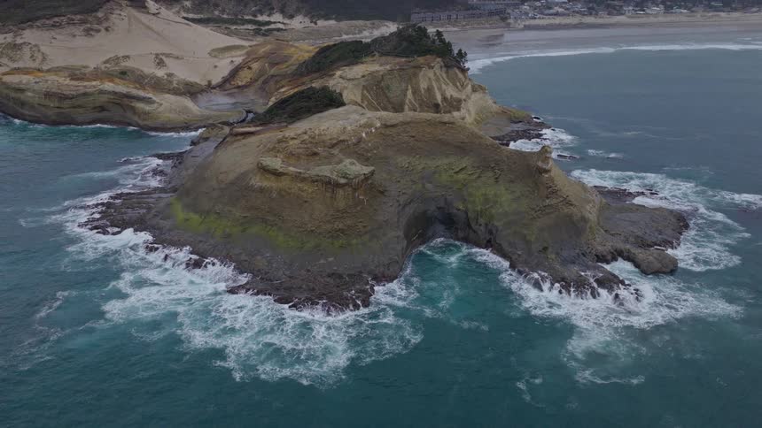 A majestic aerial view slowly pulls back to reveal the rugged beauty of the Oregon coast's Cape Kiwanda on an overcast day