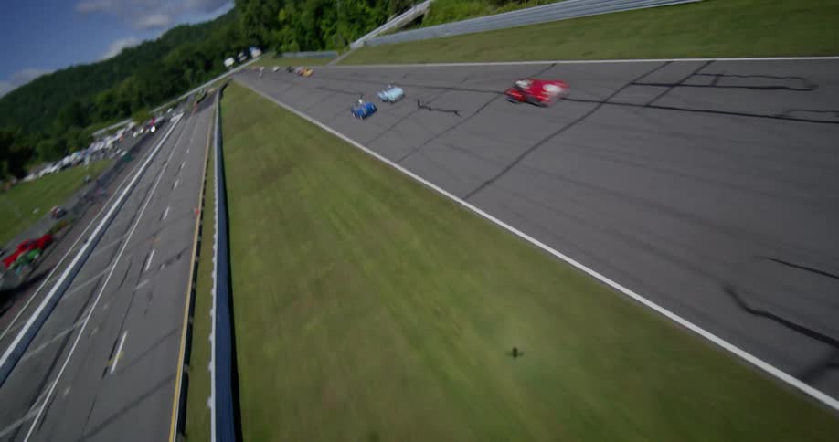 An exciting aerial view follows a pack of vintage race cars as they speed down the main straight at the famous Lime Rock Park racetrack