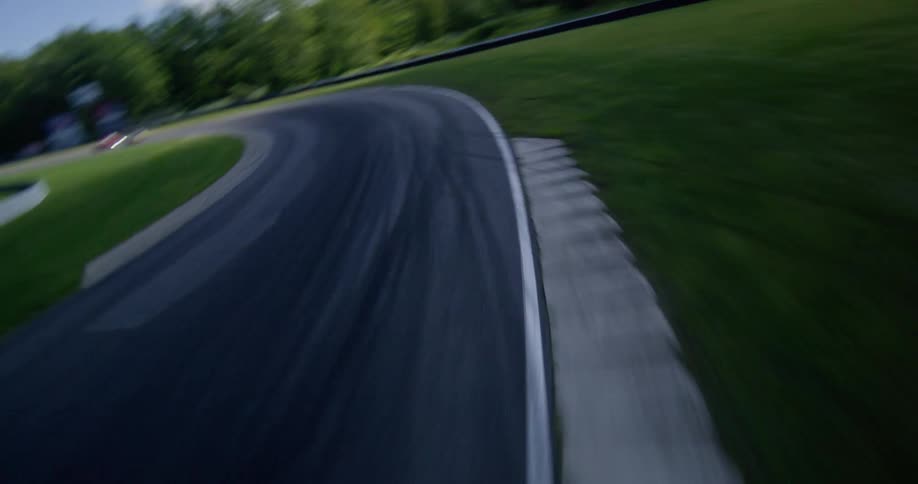 A fast-paced FPV drone chases several vintage cars racing around a winding track on a sunny day