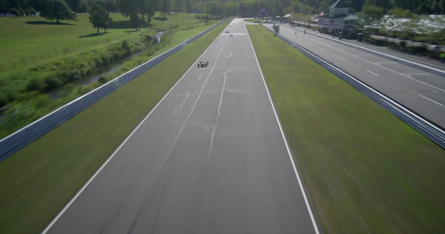 Dynamic aerial shot follows a vintage formula race car speeding down the main straightaway at Lime Rock Park