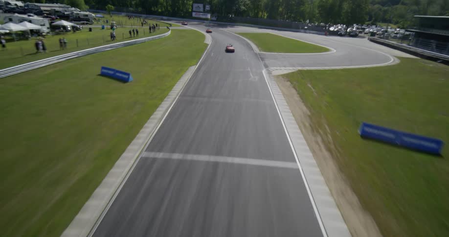 Dynamic aerial footage follows classic sports cars as they race at high speed along a winding track in the countryside