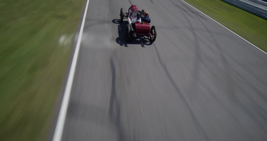 An exciting aerial shot tracks a vintage red race car as it speeds around the Lime Rock Park racetrack on a sunny day