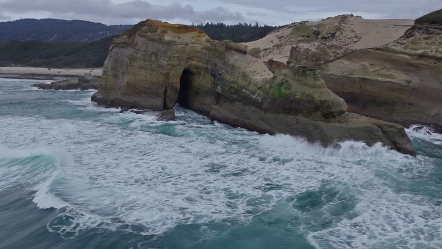 An aerial view circles the majestic sea stacks, arches, and caves of a rugged coastline on an overcast day