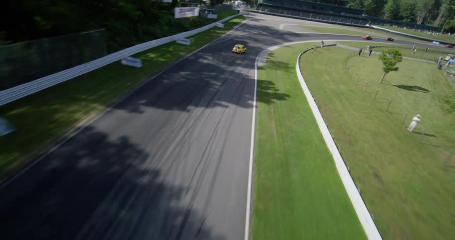 Dynamic aerial follow shot reveals a yellow sports car speeding along a professional racetrack surrounded by lush green forest