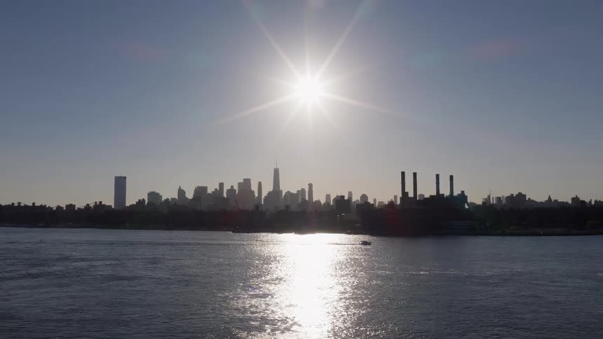 A stunning aerial view pulls back from the silhouetted New York City skyline as the sun shines brightly over the East River