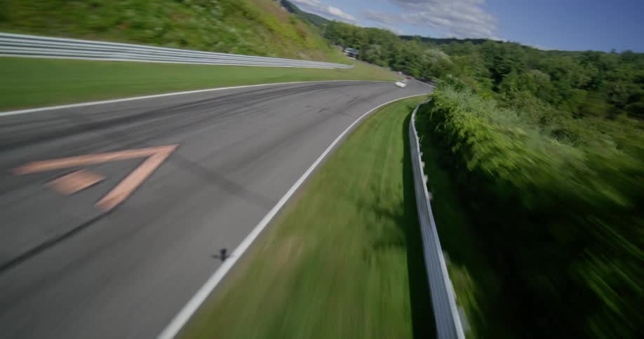 A thrilling aerial shot follows several vintage race cars speeding around a curvy track surrounded by lush green hills