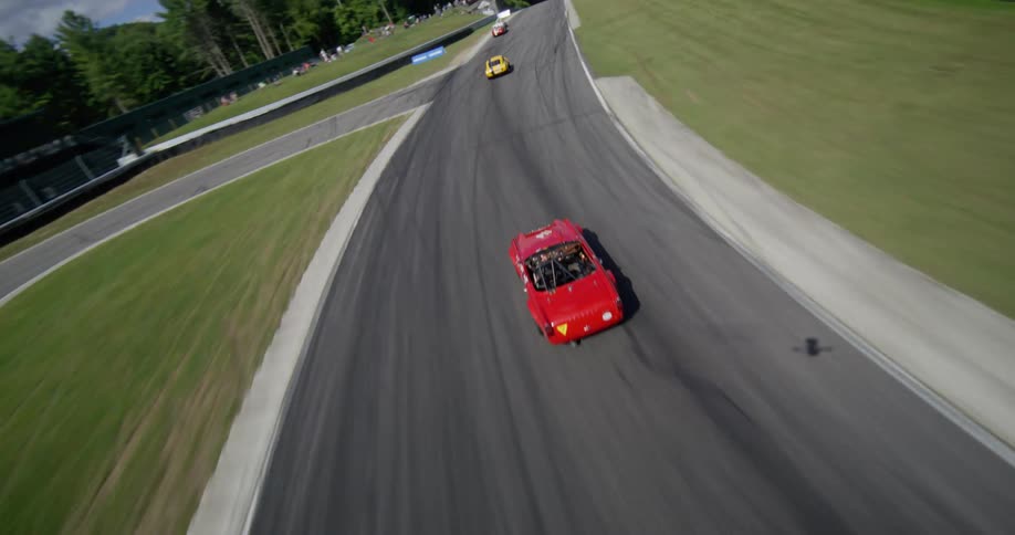 Dynamic aerial view follows vintage sports cars as they speed around a winding racetrack on a sunny day