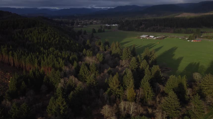 An aerial view captures the dramatic contrast between a clear-cut hillside and a vibrant green valley with forests and farmland at sunset