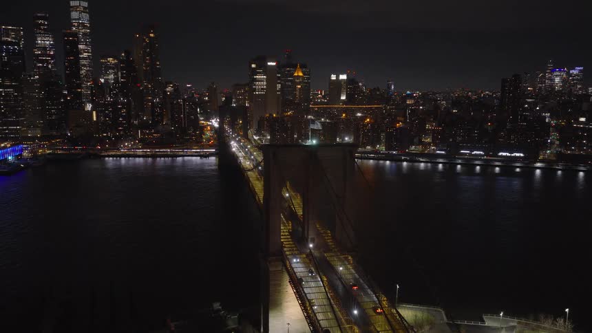 A beautiful aerial view rises over the iconic Brooklyn Bridge at night, with the illuminated Manhattan skyline in the background