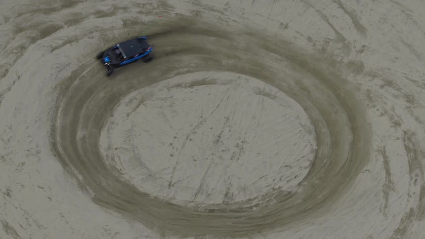 A mesmerizing top-down aerial view of a blue UTV driving in hypnotic circles inside a large sand pit while a person films