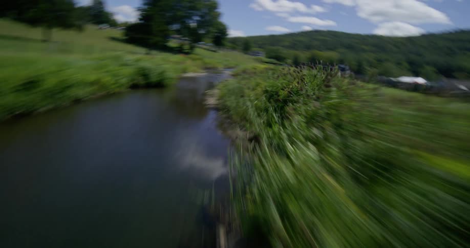 An exhilarating FPV drone flight dives down from the trees, follows a river, and then chases race cars speeding along the Lime Rock Park racetrack