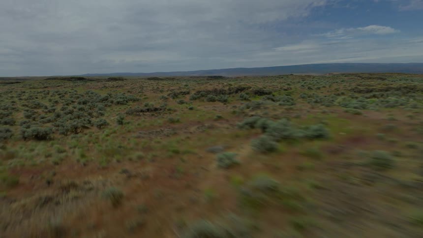 A dramatic aerial view pulls back from a serene lake in a rugged canyon to reveal the vast, arid landscape of the surrounding plateau