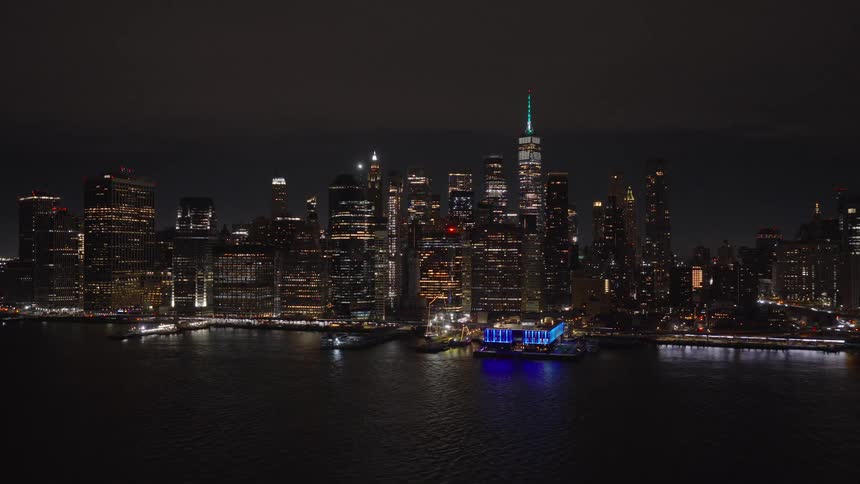 A static view of the illuminated Lower Manhattan skyline and One World Trade Center at night from across the East River