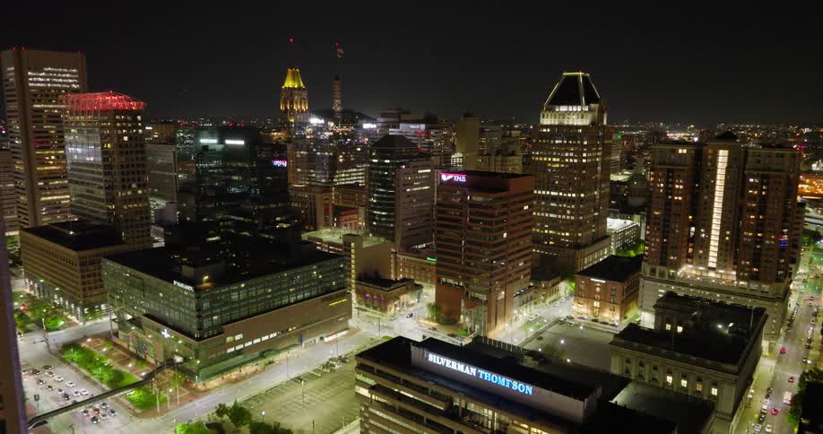 An aerial view slowly pushing in on the brightly illuminated skyline of downtown Baltimore, Maryland at night