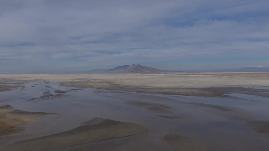 An aerial view slowly drifts over the serene, shallow waters and salt flats of the Great Salt Lake in Utah, revealing a vast and tranquil landscape with distant mountains